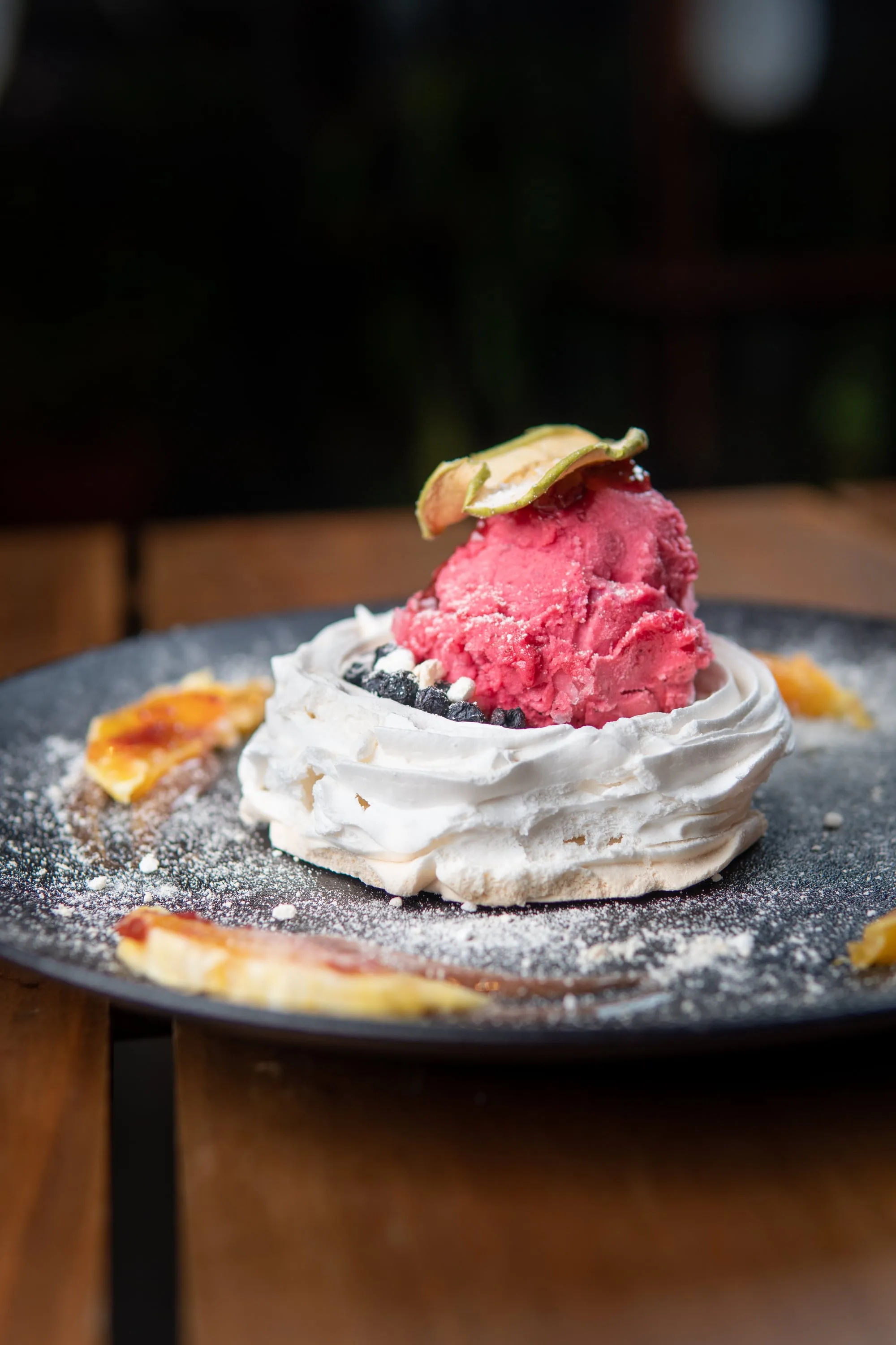 Pavlova con helado de frambuesa y una lámina de fruta deshidratada, espolvoreada con azúcar flor
