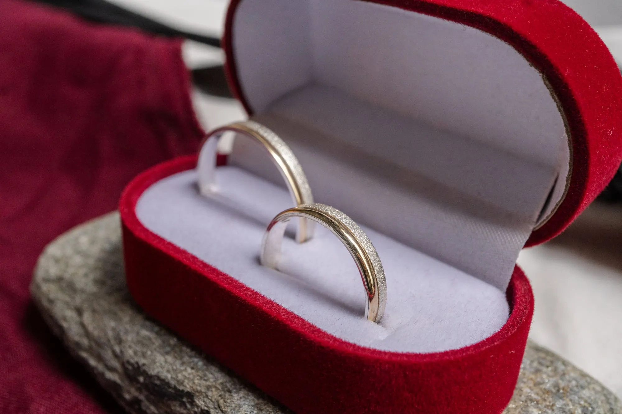 Par de argollas de matrimonio en un estuche de terciopelo rojo apoyado sobre una piedra